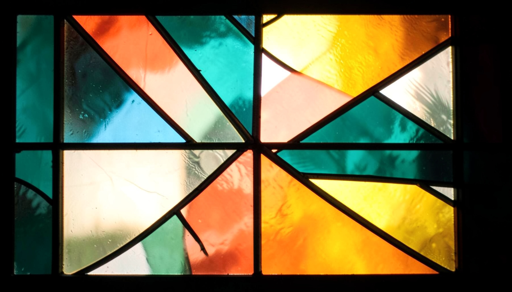 A stained-glass composition with bold leaded segments in deep teal, coral, and amber, forming abstract geometric shapes against a luminous backdrop