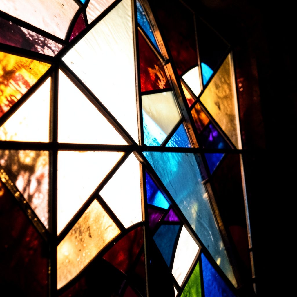 A small stained-glass profile roundel in teal and mint with bold black leading, warm coral highlights framing the shape.