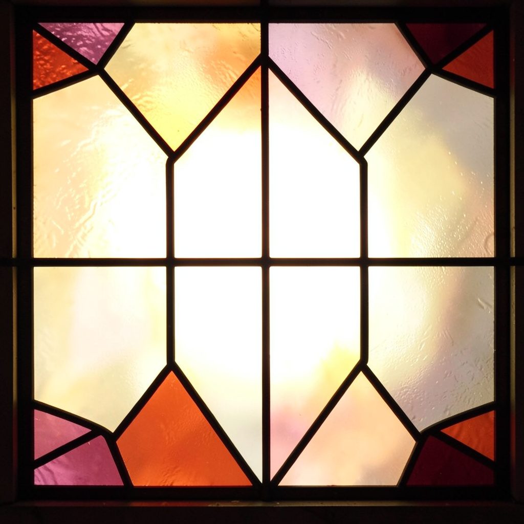 A stained-glass panel of interlocking angular shapes in teal, mint, and coral, with thick black lead lines forming a structured grid-like pattern suggesting infrastructure and connectivity.